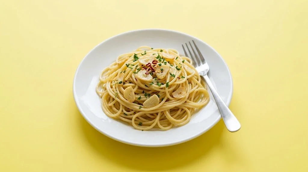 A plate of spaghetti with garlic oil, garlic slices, chili flakes and parsley on a yellow background