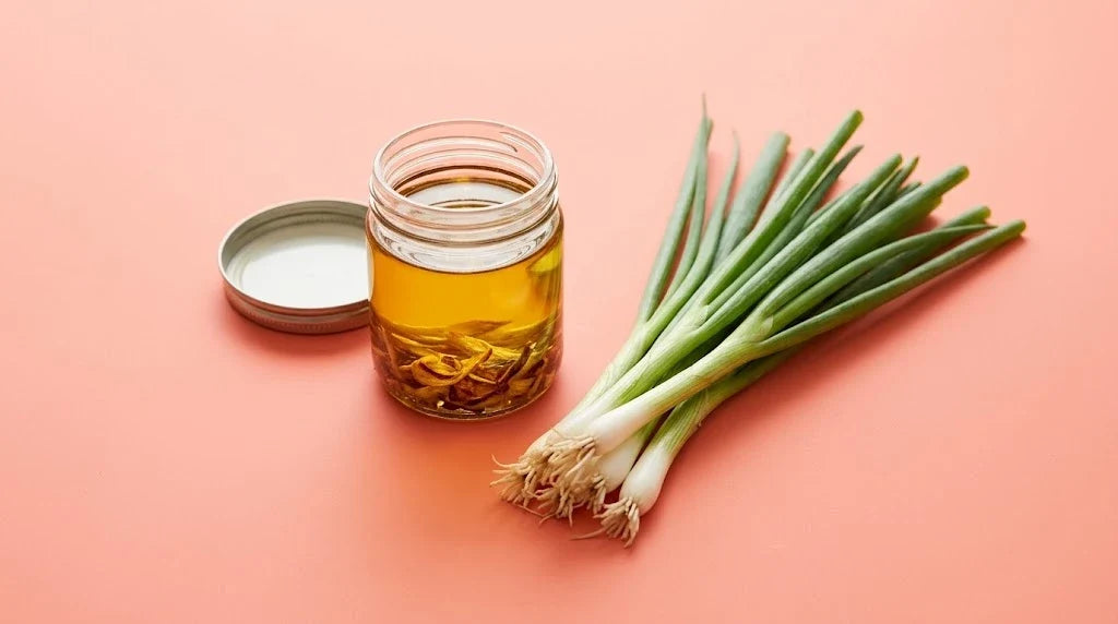 A jar of golden scallion oil with crispy scallions beside fresh spring onions on a coral background